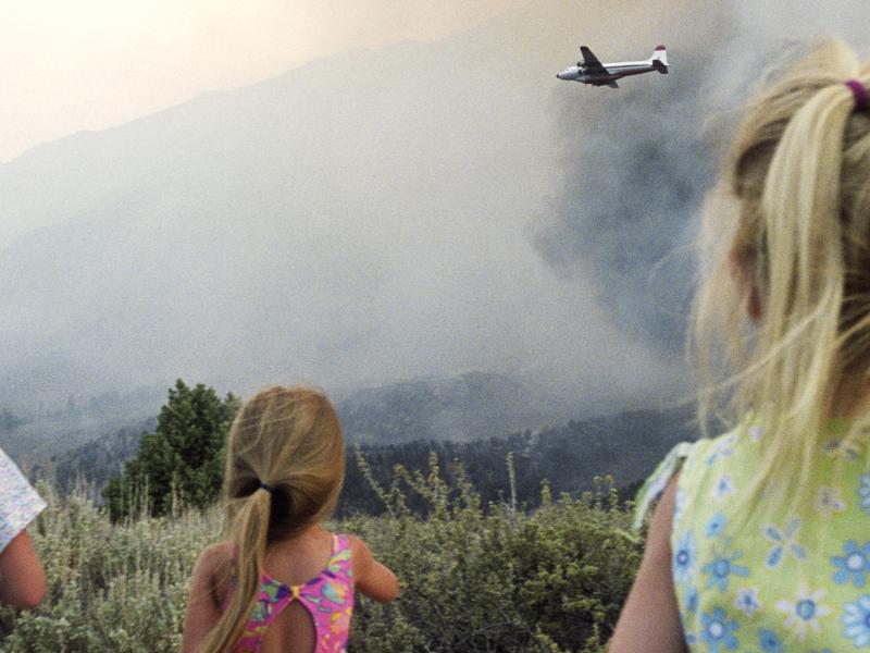 Kids looking at plane and fire in distance