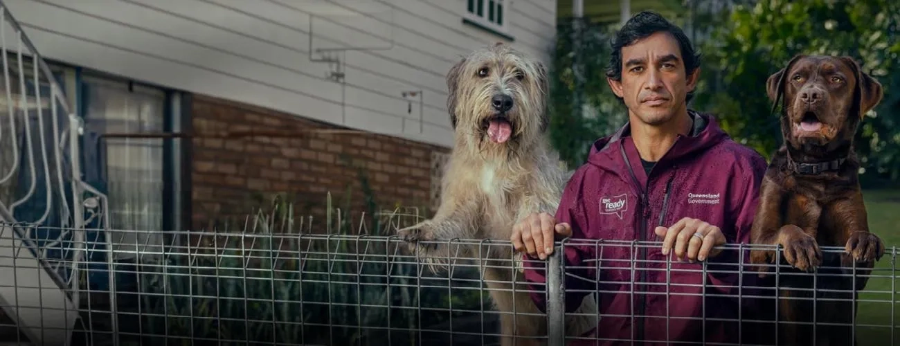 Johnathan Thurston leaning on a chain link fence with two dogs either side